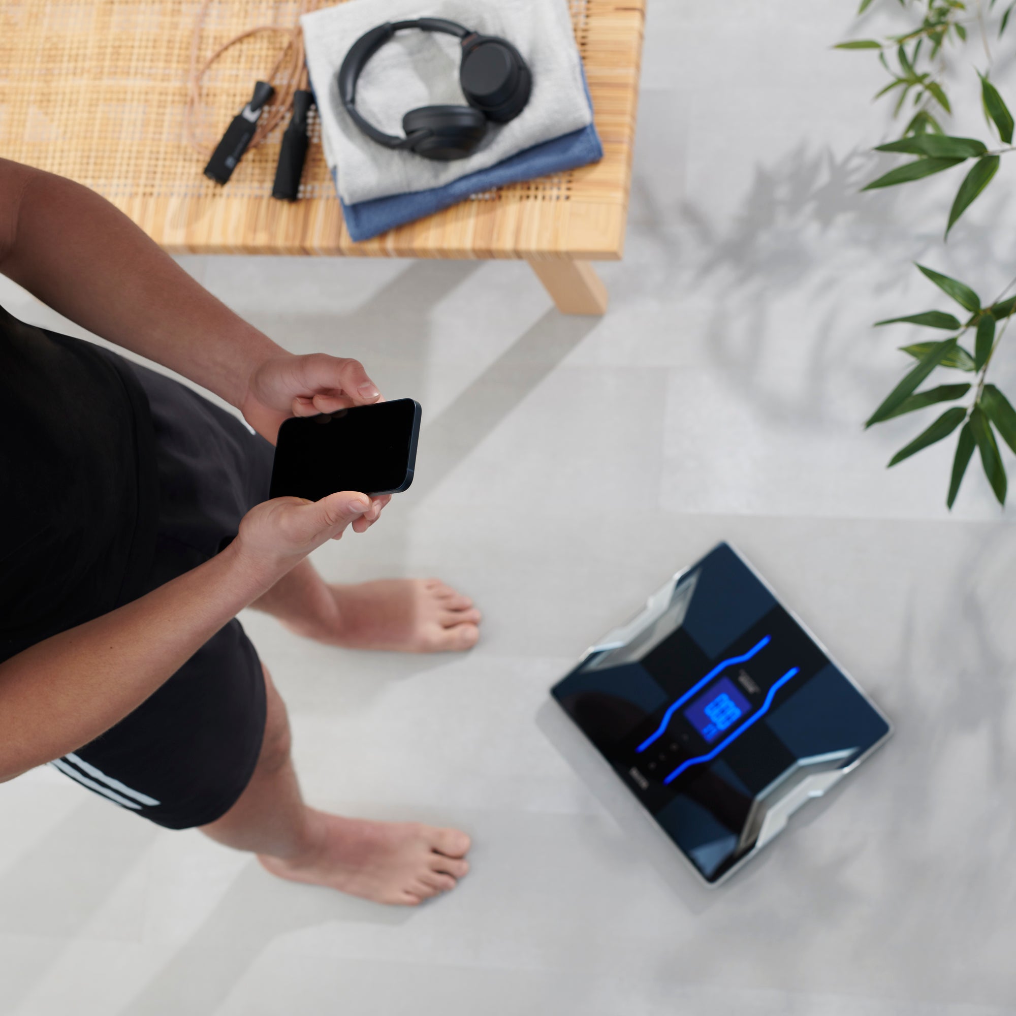 Person using a smartphone app on a black Tanita RD-953 Bluetooth Body Composition Monitor in a home setting.